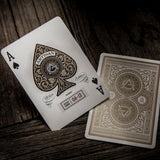 Two playing cards, an Ace of Spades and the gold design on the back of another, on a wooden surface.
