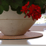 White ceramic planter with red flowers on a cork coaster