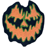 A Halloween-themed chainstitch patch featuring a spooky jack-o'-lantern face. The design has a dark navy blue base, orange textured facial features, and green stitched outlines, presented on a clean white background.