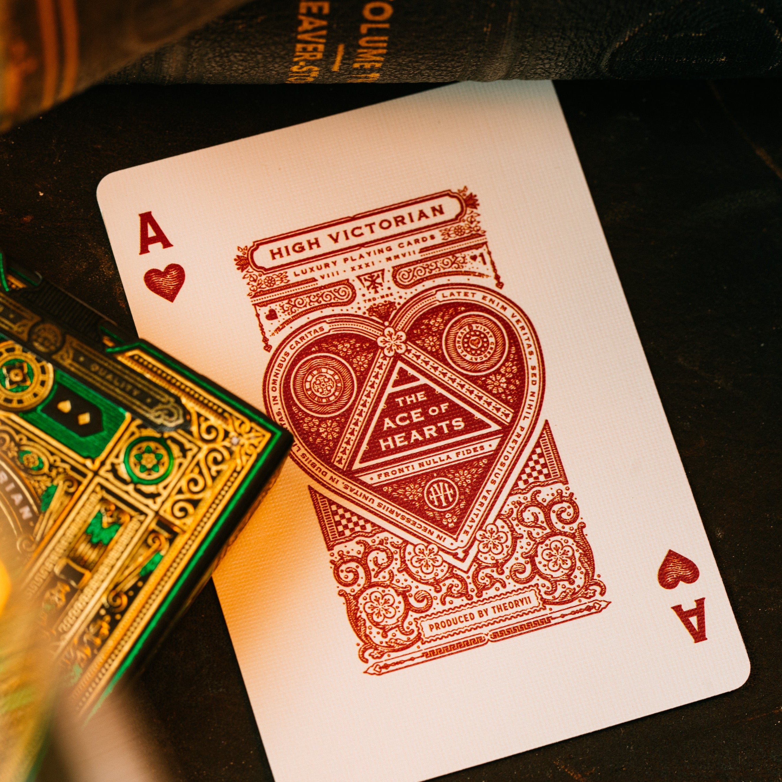 Playing cards with a red heart suit card and green and gold card box on a dark surface.