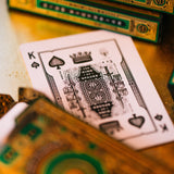 Close-up of a playing card with intricate design, surrounded by green and gold playing card boxes.