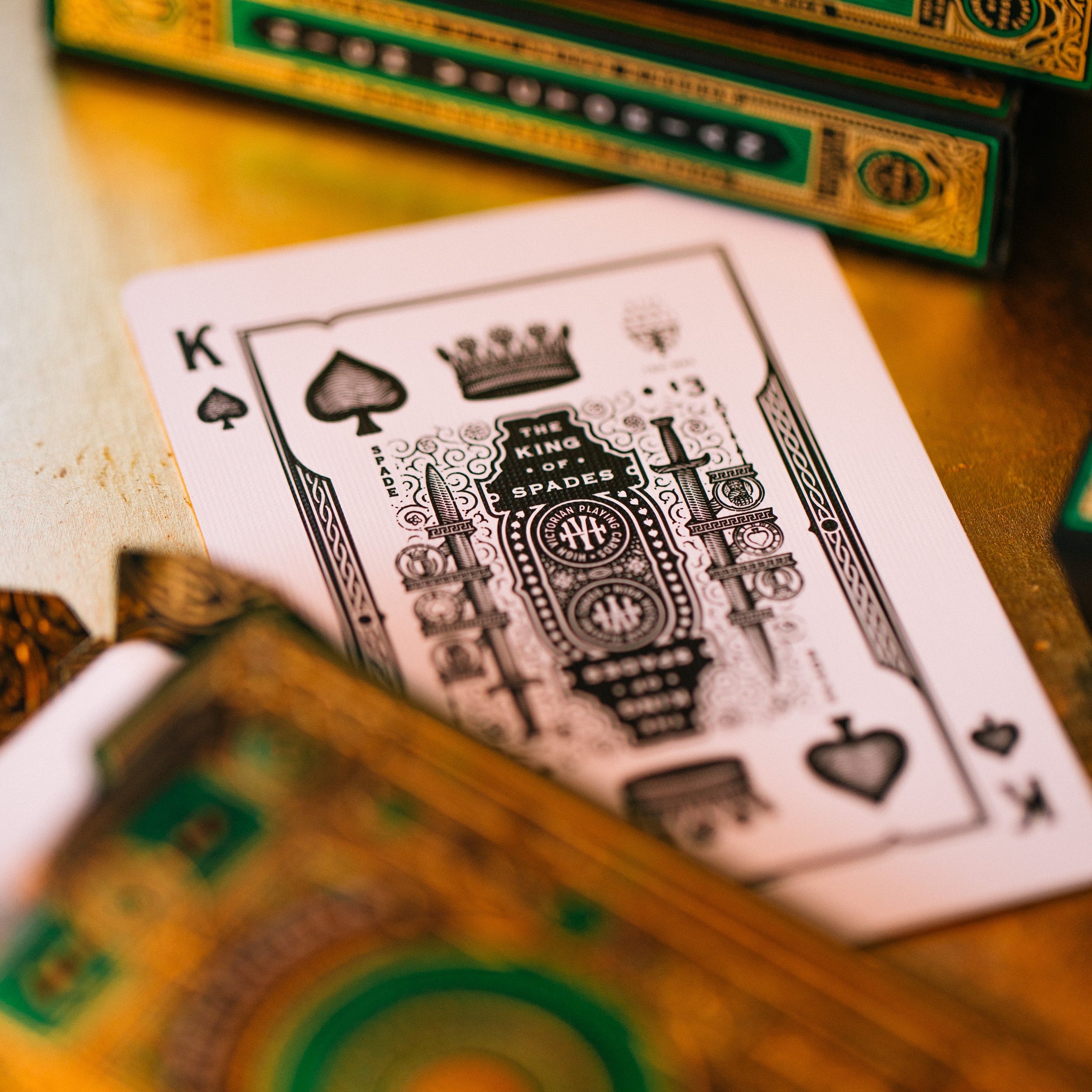 Close-up of a playing card with intricate design, surrounded by green and gold playing card boxes.