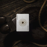 Card with an eye design on a dark wooden surface with ropes
