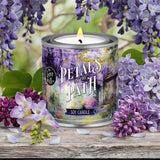 Candle labeled 'Petals on the Path' surrounded by purple flowers on a wooden surface