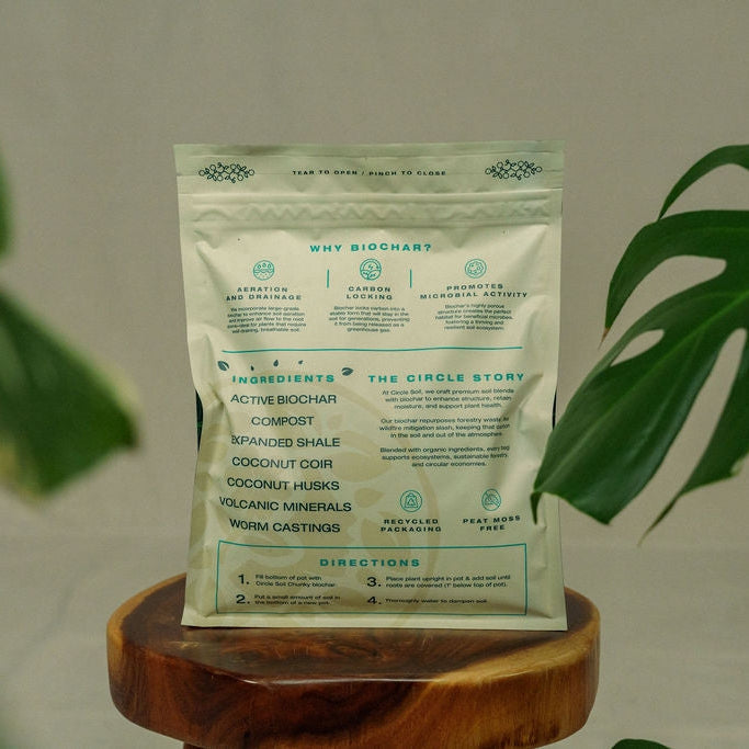 Biochar product packaging on a wooden stand with green leaves in the background