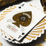 Playing cards with gold and black design on a white surface with coins.