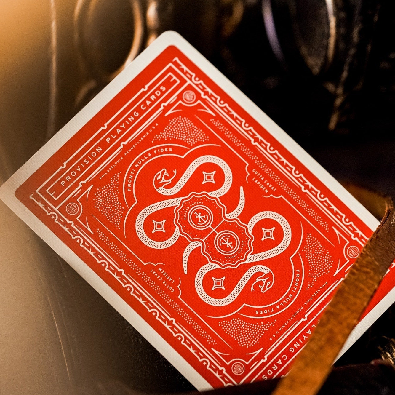 Red playing card with intricate design held by a metallic tool