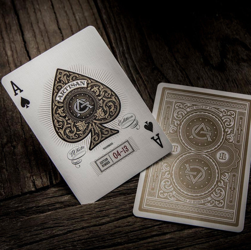 Two playing cards, an Ace of Spades and the gold design on the back of another, on a wooden surface.