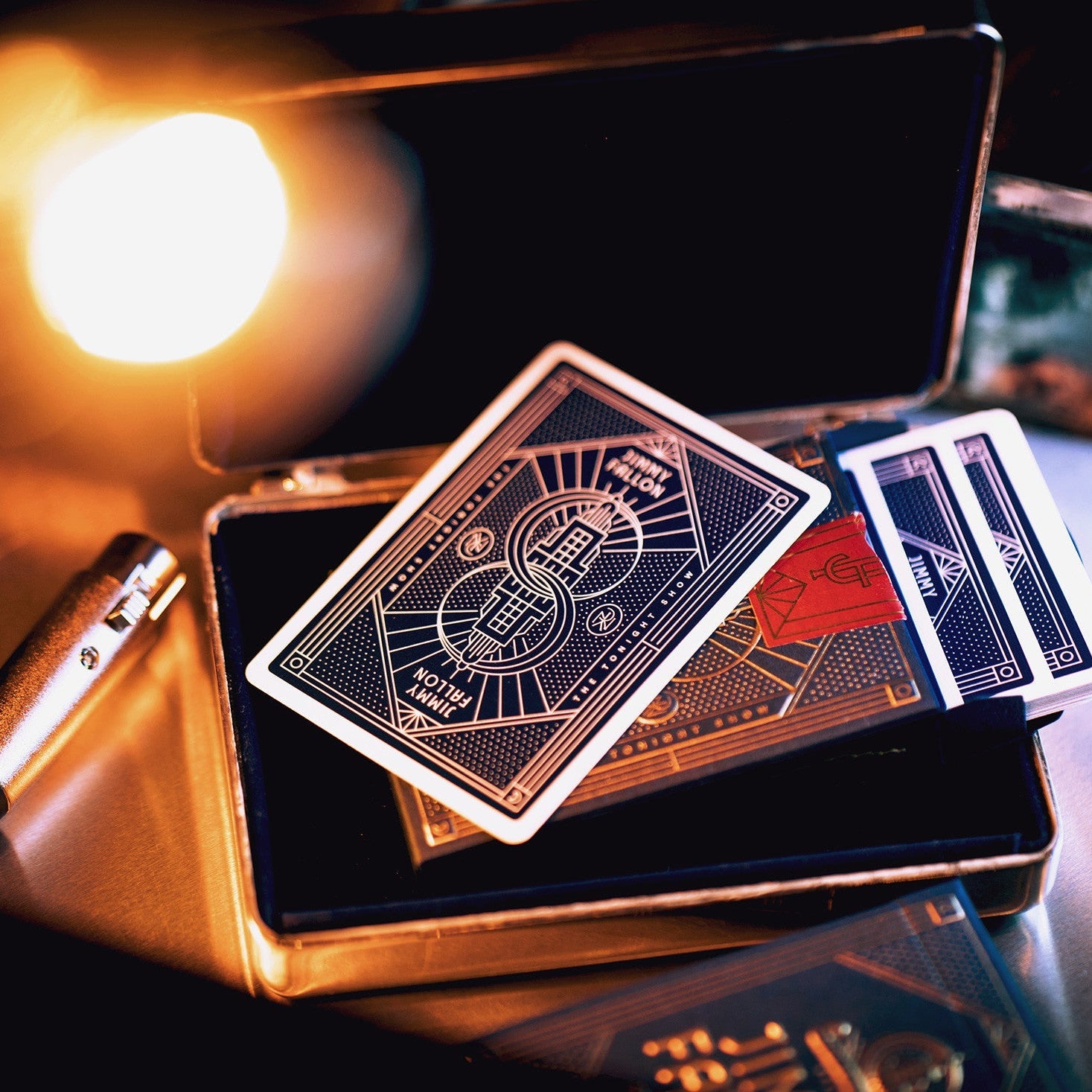 Playing cards with an Art Deco design on a metallic box under warm lighting.
