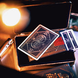 Playing cards with an Art Deco design on a metallic box under warm lighting.