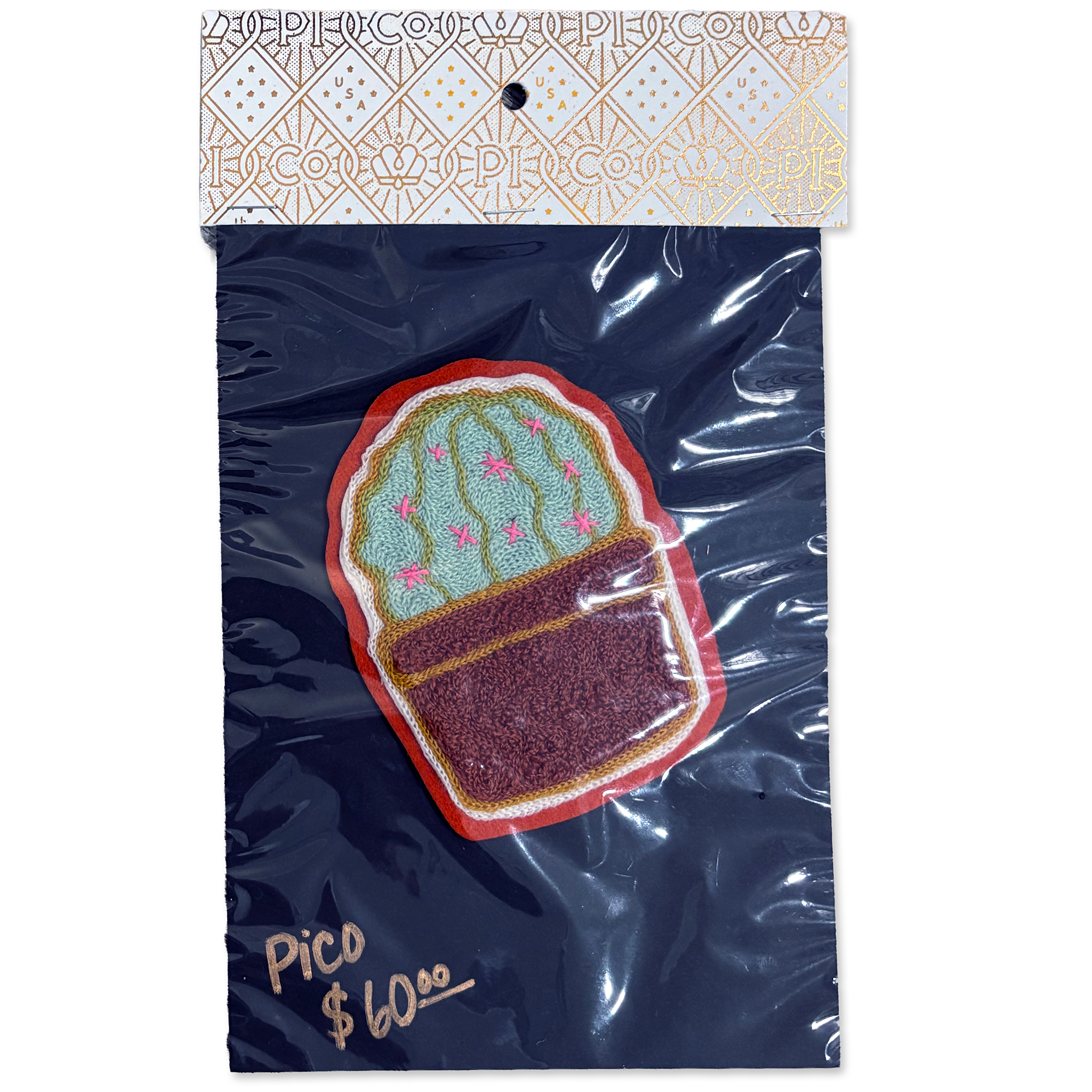 An embroidered cactus patch in a pot, packaged in a clear plastic bag with a branded header card. The patch features a green cactus with pink details and a dark brown pot, set against a dark navy blue backing card with gold foil text and a patterned top.