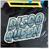 A 'DISCO QUEEN' embroidered patch with a glittery light blue and yellow patterned fill, outlined in white and black, shown inside its clear plastic packaging with a colorful header card.