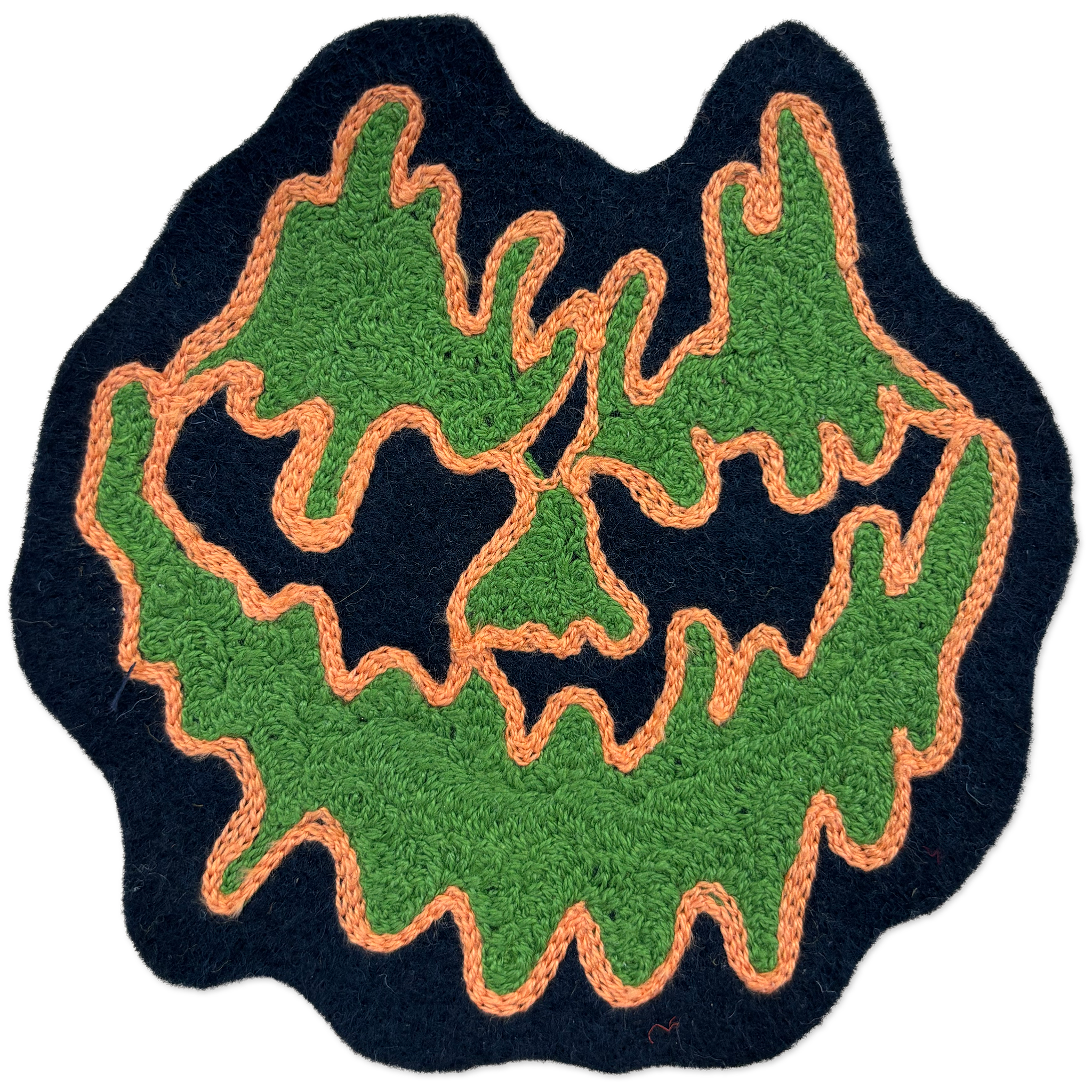 A handmade felt patch shaped like a jack-o'-lantern face, featuring textured green felt for the cheeks and forehead, black felt for the eyes and nose, and orange yarn trim outlining the design, set against a plain white background.
