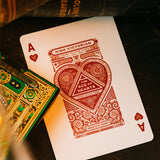 Playing cards with a red heart suit card and green and gold card box on a dark surface.