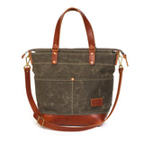 A dark gray waxed canvas tote bag with brown leather handles, trim, and a matching adjustable shoulder strap, shown against a plain white background.