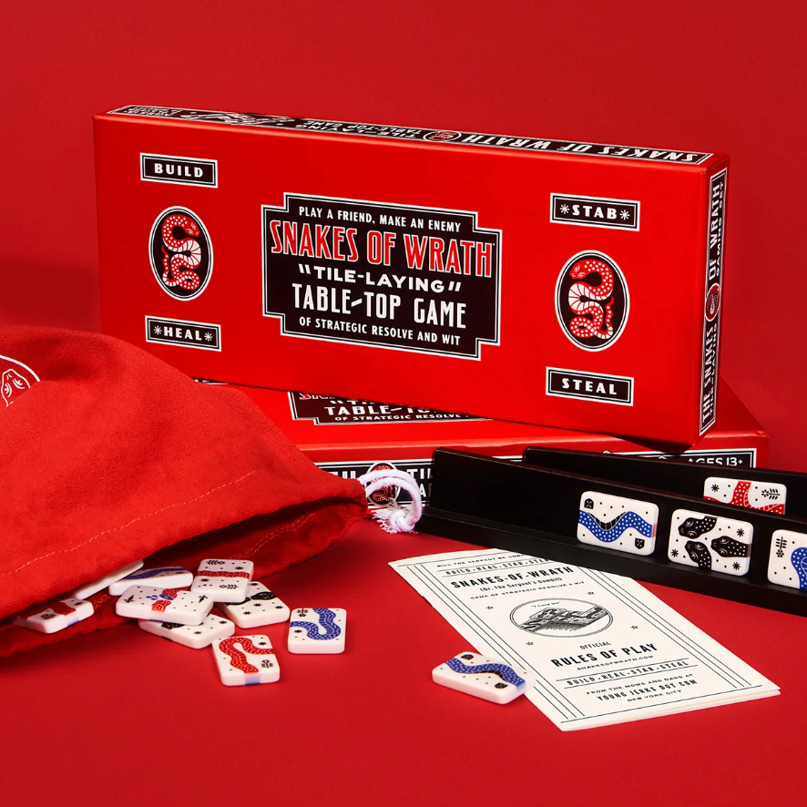The image shows the components of the 'Snakes of Wrath - Tabletop Game'. This includes a red box with the game title, a custom canvas snake sack, various game tiles, and two wooden privacy racks.