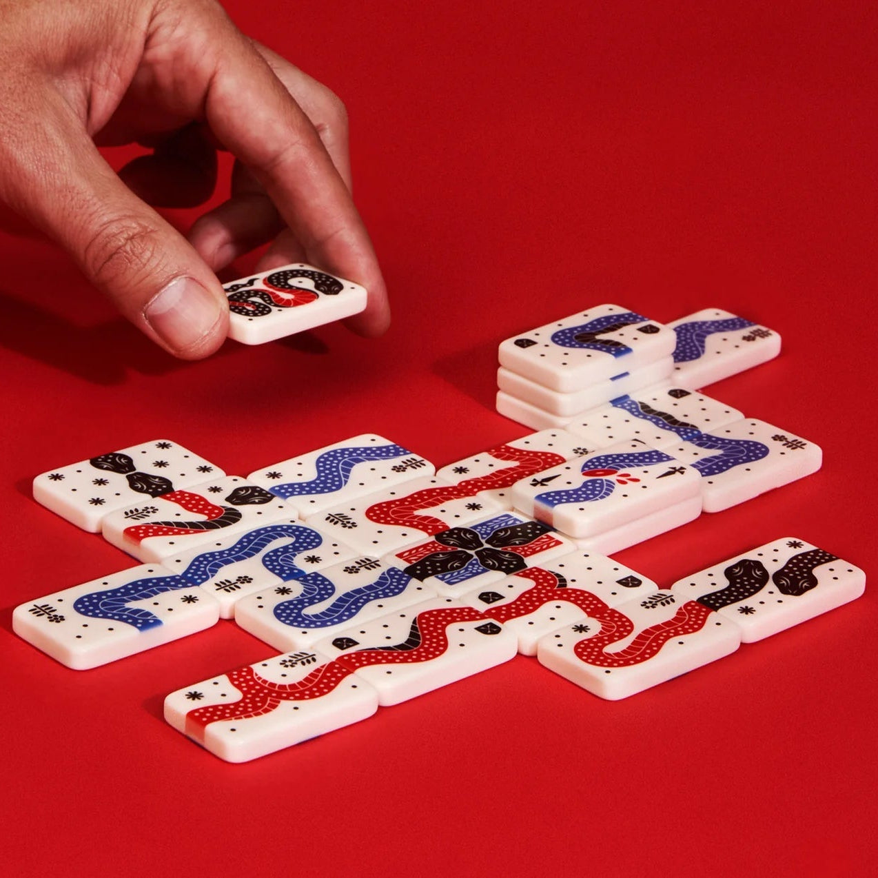 A hand placing a tile in the Snakes of Wrath game, on a red background