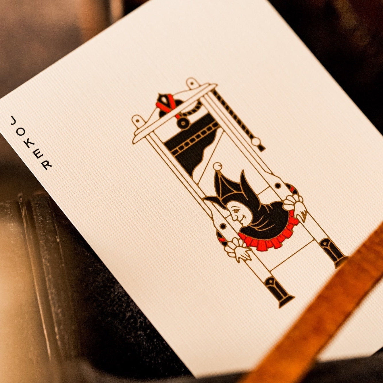 Playing card with a joker and guillotine design on a wooden surface