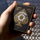 Hand holding a deck of black playing cards with gold design