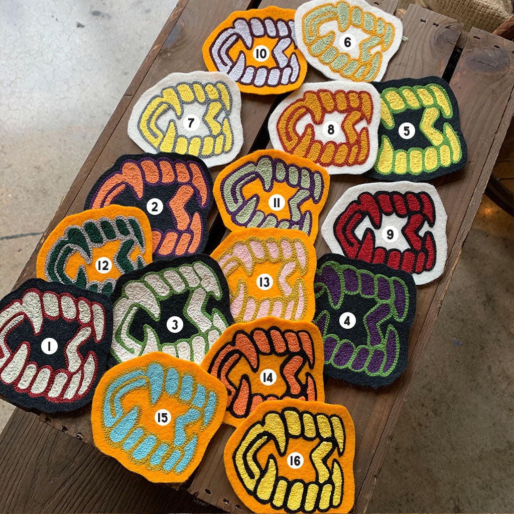 A collection of various chainstitch patches laid out on a wooden surface, predominantly in colors related to Halloween such as black, orange, green, and red.