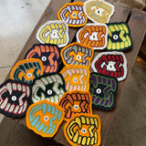 A collection of various chainstitch patches laid out on a wooden surface, predominantly in colors related to Halloween such as black, orange, green, and red.