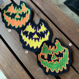 Three hand-made chainstitch patches depicting jack-o-lantern faces in various colors.