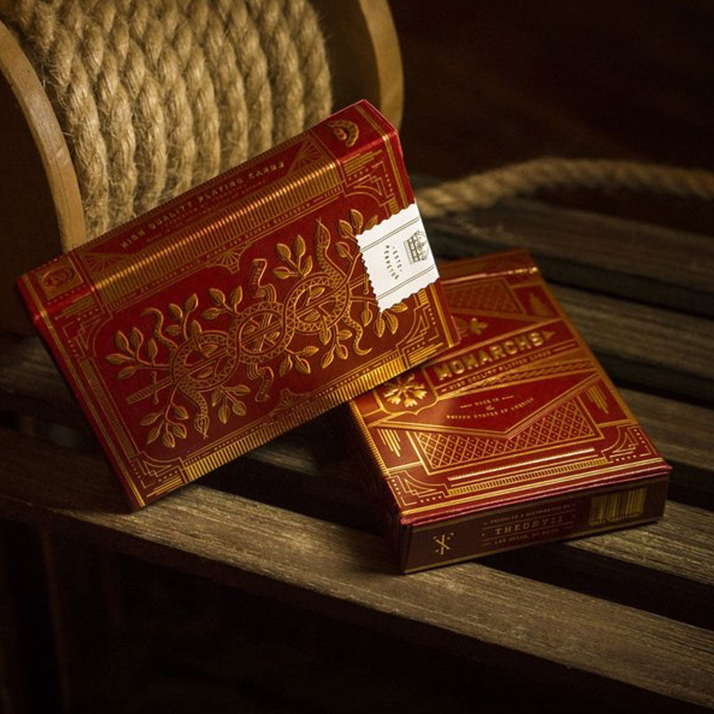 Two red decks of Monarch playing cards, on a wooden crate with rope in the background.